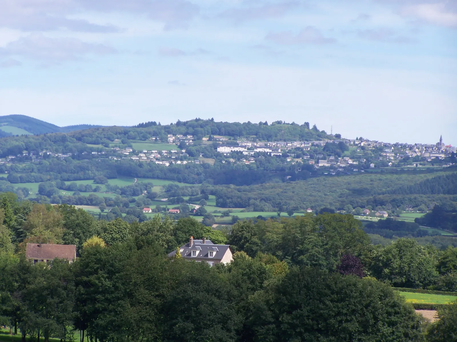Château-Chinon sur sa colline, vue depuis Dommartin : les maisons et le clocher de la ville au-dessus des forêts et des prés du Haut Morvan