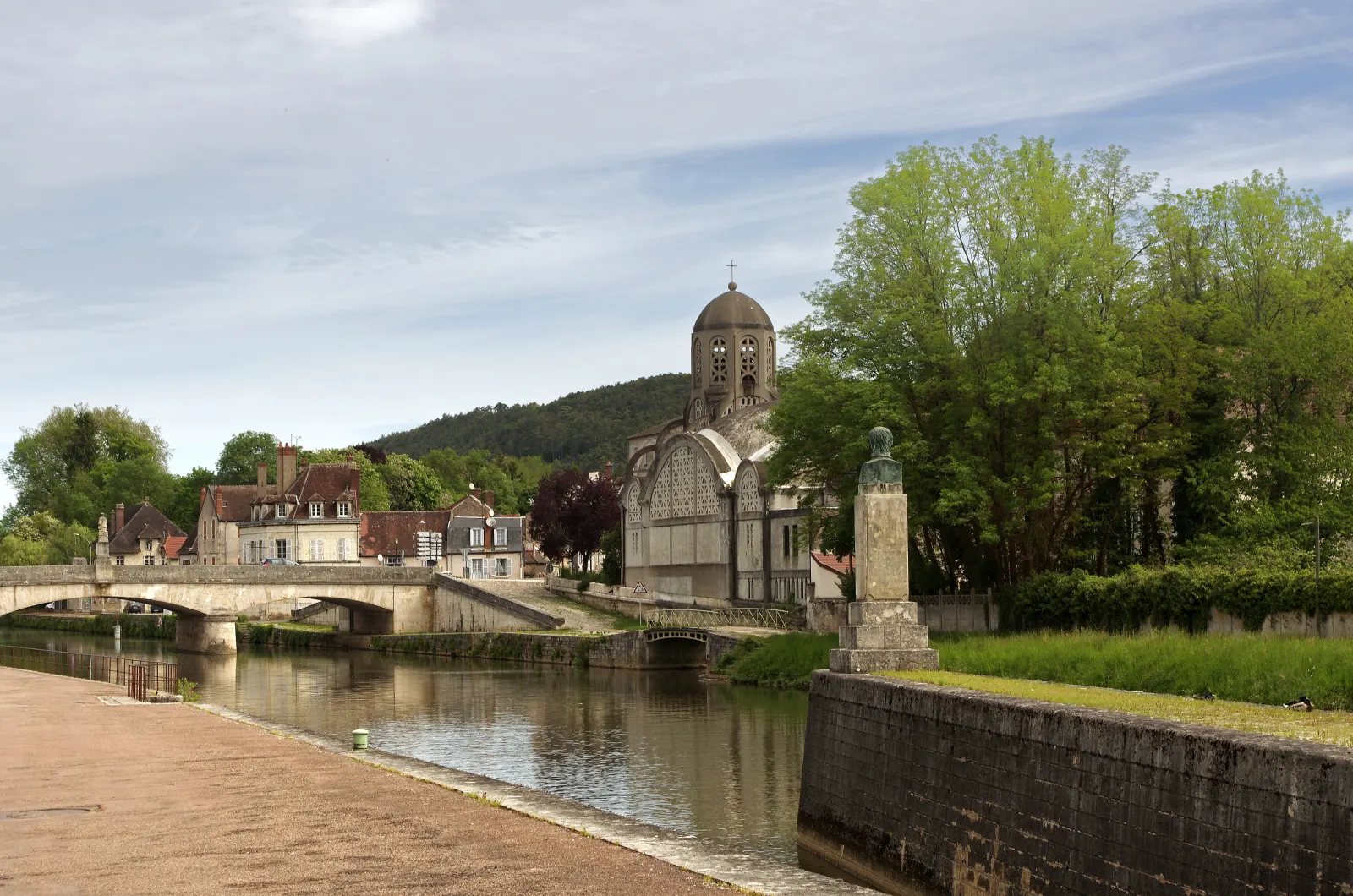 Le pont de Bethléem et l’église Notre-Dame de Bethléem à Clamecy, vus depuis le quai, au bord de l’eau, sous un ciel de printemps